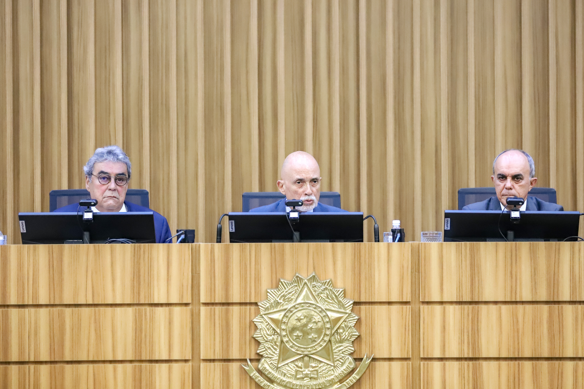 presidente Samuel está sentado à mesa alta, no centro, falando ao microfone, com os ministros Aloysio Veiga à sua esquerda, e Claudio Brandão, à direita
